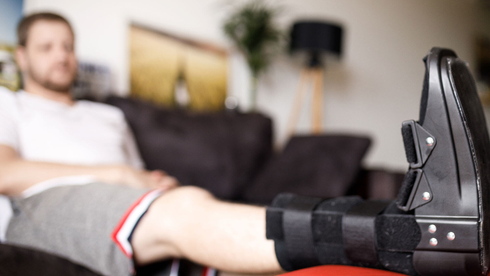 Person resting with leg in boot, journaling on couch during recovery